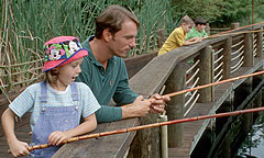 Fishing A father and daughter fish from a wooden bridge with cane fishing poles.