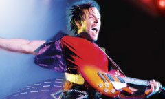 Live band with purple mood lighting on stage performing in front of a crowd